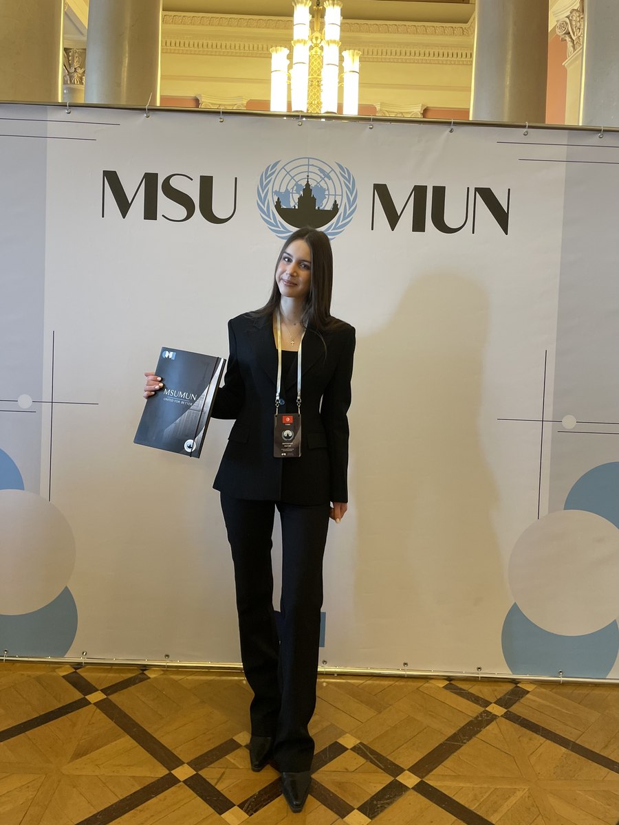 Mariia Miroshnik posing with the MSUMUN delegate folder in front of the event backdrop
